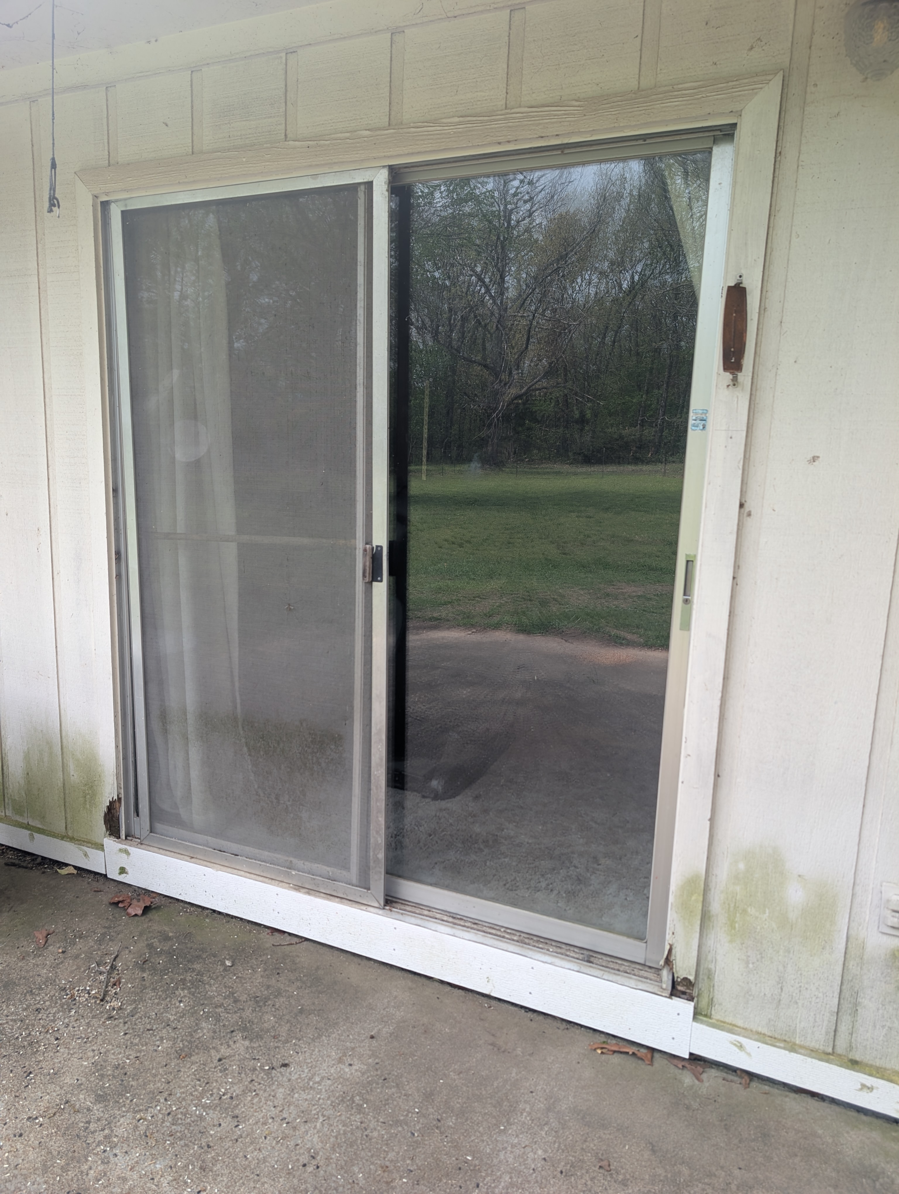 Before Door & Trim Replacement — Aging sliding patio door with rusted rail, rotting frame beneath the threshold, and deteriorated trim
